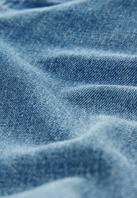 Tissu en denim bleu avec une texture lisse, présentant des motifs de tissage diagonaux subtils et quelques légères marques éparpillées.