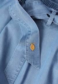 Ανοιχτό μπλε denim πουκάμισο με μυτερό γιακά και μικρή κίτρινη κεντημένη λεπτομέρεια φύλλου κοντά στη γραμμή του λαιμού.