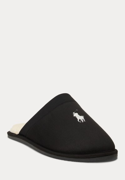 Schwarzer Slip-on-Hausschuh mit weiß besticktem Pferdelogo und weichem weißem Innenfutter, schräge Ansicht auf einfarbigem Hintergrund.