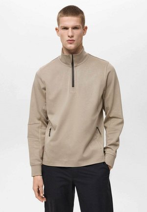 Beige pullover with a half-zip front, long sleeves, and side zippers. Made from soft fabric with a smooth texture and minimal design.