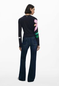 T-shirt à manches longues avec un corps bleu marine foncé et un motif floral sur la manche droite. Associé à un jean en denim foncé évasé et des chaussures décontractées.