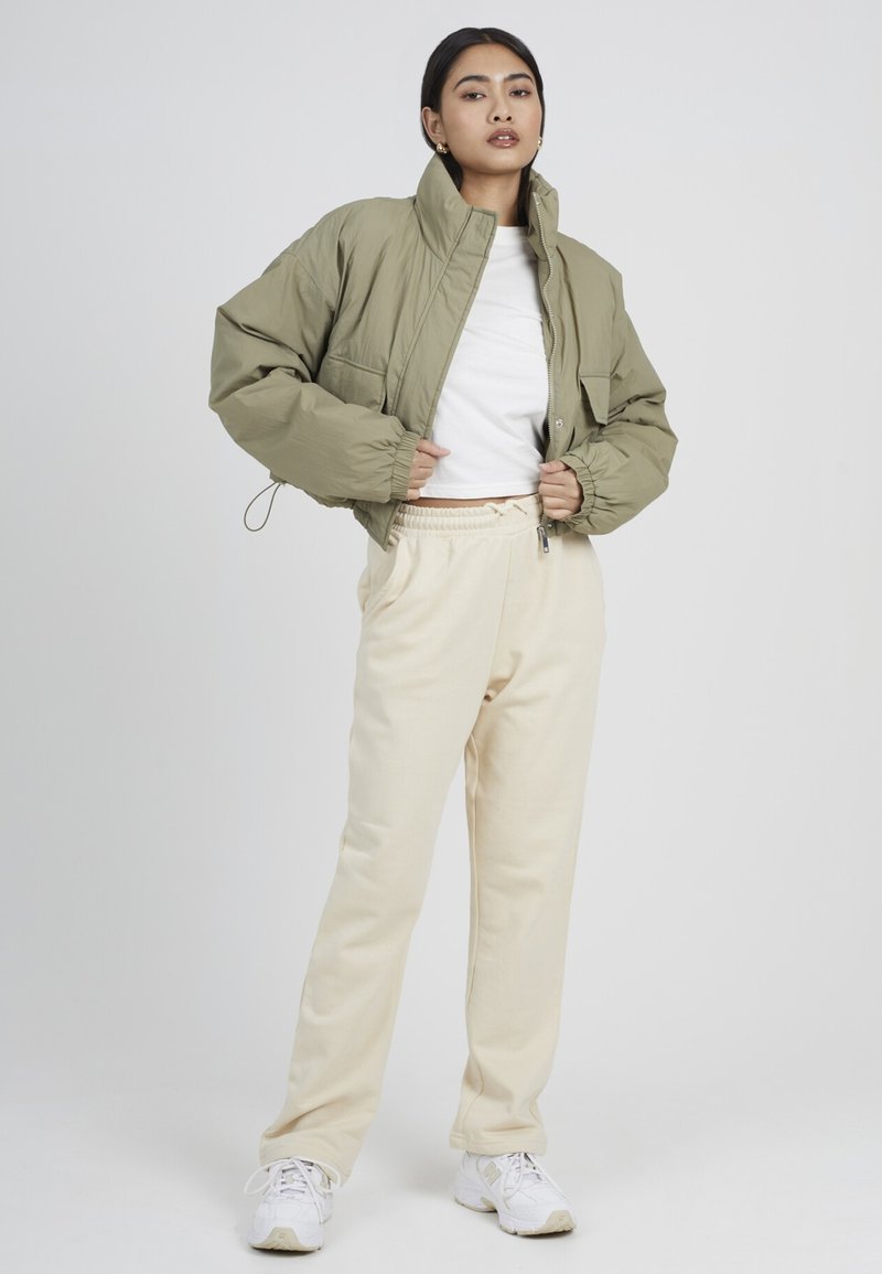 Chaqueta acolchada verde, corta, con cuello alto, combinada con pantalones de chándal crema y zapatillas blancas. Tejido suave y ajuste relajado.