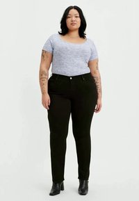 Calças de ganga pretas de cintura alta com um corte justo, combinadas com uma blusa de manga curta em roxo claro que possui um padrão texturizado. Botins pretos de salto.