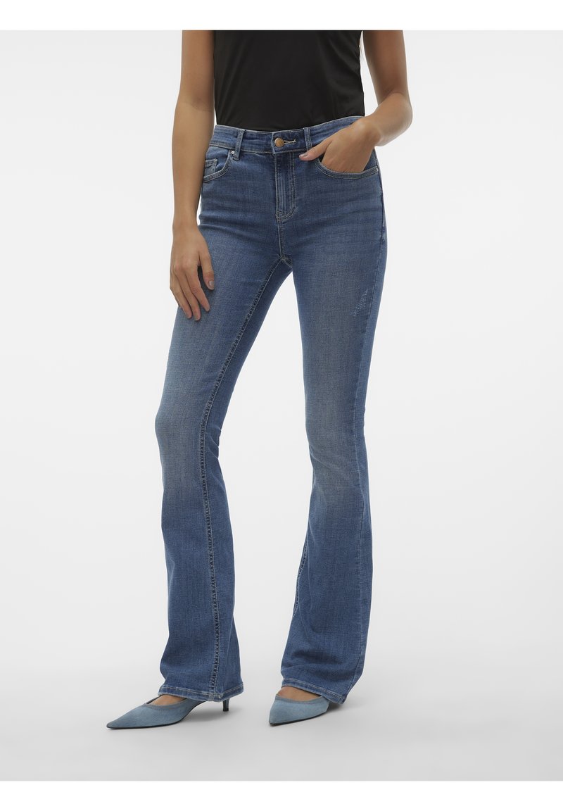 Blå utsvängda jeans i denimtyg med medeltvätt. Har fem fickor, bältesöglor och knappstängning, tillsammans med blå spetsiga klackar.