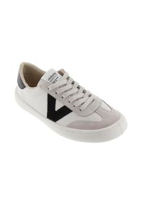 Sneaker bianco e grigio chiaro con una "V" nera sul lato, linguetta beige sul tallone, lacci bianchi e suola bianca, inclinato per mostrare la parte anteriore e laterale.