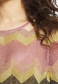 Textured knit top featuring chevron pattern in pink, gold, and black hues. The design has a scoop neckline and sheer finish.