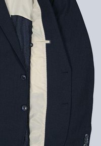 Navy pinstriped blazer with a cream-colored lining, two front buttons, and detailed cuff buttons, featuring structured shoulders and a smooth texture.