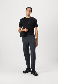 Camiseta negra de manga corta, pantalones gris con un patrón y cintura elástica, bolso negro de bandolera, y zapatos negros con cordones.