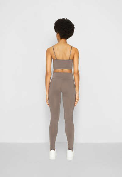 Conjunto de top desportivo e leggings castanho, feito de material elástico. Apresenta alças finas e uma cinta alta. Os sapatos são brancos, de estilo plataforma.