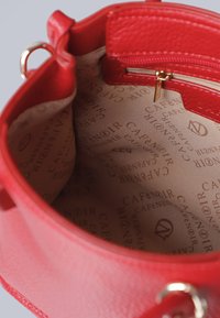 Interieur van een rode leren handtas met een gladde textuur, een opvallend ritscompartiment en een bedrukte logopatroon op de voering.