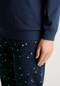 Navyblauwe katoenen sweatshirt gecombineerd met sterrenpatroon navy pyjamabroek. Zachte textuur, relaxed ontwerp en elastische manchetten.