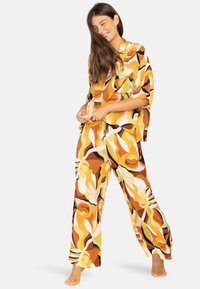 Mønstret loungewear sæt i flere farver med en løs pasform i toppen og vidde benbukser, lavet af tekstureret stof med et abstrakt bladmønster i varme nuancer.