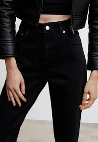 Czarne jeansy z wysokim stanem, wykonane z gładkiego denimu, wyposażone w zapięcie na guzik, szlufki na pasek oraz dekoracyjne przeszycia na kieszeniach.