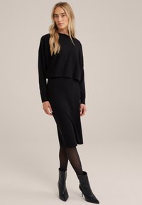 Completo in maglia nera composto da un maglione corto e una gonna midi a coste, abbinato a stivali neri con punta.