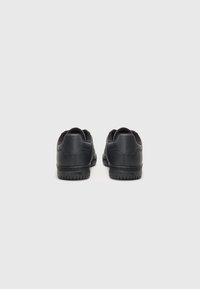 Svarte sneakers med glatt lær øvre, rund tå, polstret krage og teksturert gummisåle. Har minimalistisk design og subtil merkevare.
