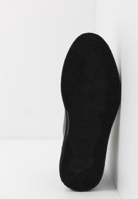 Černá podrážka s texturovaným gripem a embosovaným logem "Calvin Klein". Hladké okraje a pevný materiál, navržený pro odolnost.