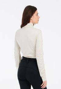 Beige dlhý rukáv top s vysokým golierom a priliehavým strihom, kombinovaný s čiernymi nohavicami s vysokým pásom, ktoré majú hladkú textúru a jemné švy.
