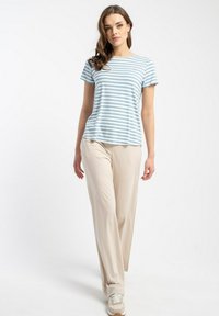Pasiasty niebiesko-biały t-shirt z krótkim rękawem w połączeniu z luźnymi beżowymi spodniami i trampkami. Koszulka ma okrągły dekolt.