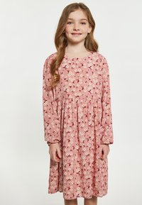 Lyserød blomsterkjole med lange ærmer og rund halsudskæring, prydet med en samlet talje, dekoreret med hvide tusindfryd og røde accenter.