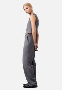 Grijze cropped mouwloze top met een gestructureerd ontwerp, gecombineerd met hoge grijze broeken. Glanzende zwarte schoenen maken de outfit compleet.