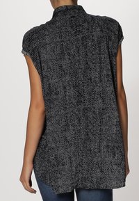 Chemise à manches courtes noir et blanc avec un col haut, présentant un tissu texturé et une coupe loose, arrivant en dessous des hanches.