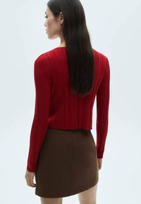 Rød ribbet strikbluse med lange ærmer og cropped snit, parret med en brun tætsiddende nederdel, der har en glat tekstur og figursyet design.