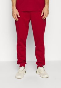 Rote Jogginghose aus weichem Stoff, mit schmal zulaufendem Bein und gerippten Bündchen. Kombiniert mit hellen Sport Schuhen.