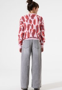 Suéter rosa y blanco con un estampado de leopardo en rojo y coral, combinado con pantalones de mezclilla grises de pierna ancha y cintura alta. Textura suave, ajuste casual.