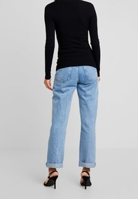 Zwart geribbelde top met lange mouwen, gecombineerd met lichtblauwe jeans met hoge taille en rechte pijpen, opgerolde zoom en zwarte sandalen met hoge hak.
