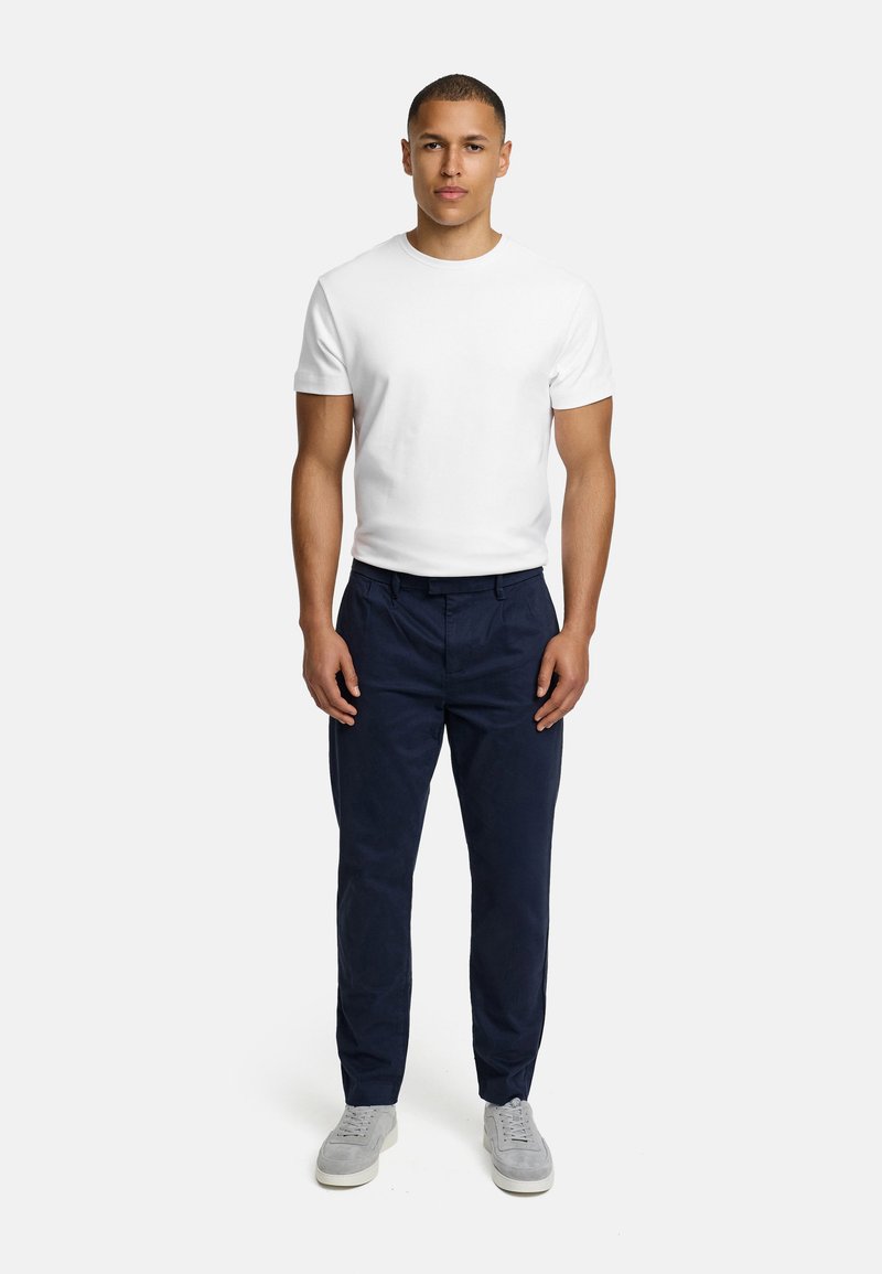 T-shirt bianca a maniche corte abbinata a pantaloni blu navy e sneakers grigie. Design semplice, materiale in cotone e taglio classico.