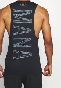 Černý tílko s velkým, texturovaným nápisem "MAN" na zadní straně. Volný střih, bez rukávů, zvýrazňující záda. Hladká textura látky.