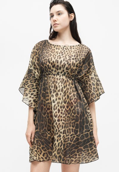 Γυναίκα που φοράει άνετο, φόρεμα μέχρι το γόνατο με φαρδιά μανίκια και καφέ-μαύρο μοτίβο λεοπάρδαλης.