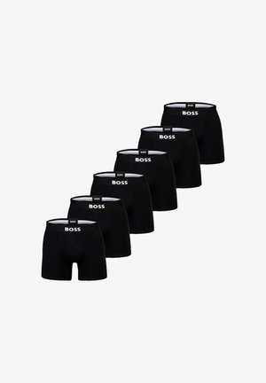 Pantalones cortos de boxeo negros exhibidos en fila, con un logo blanco en la cinturilla elástica. Tejido suave, diseño ajustado.