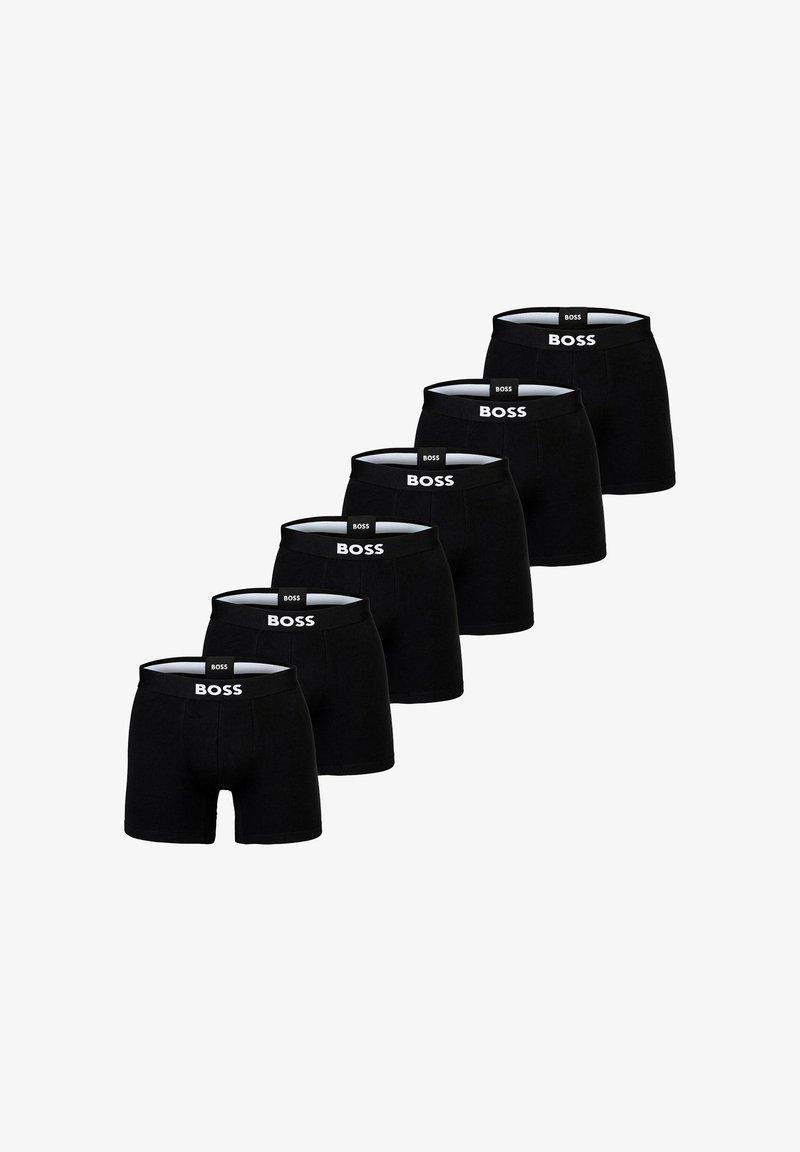 Boxers noirs exposés en rangée, avec un logo blanc sur la ceinture élastique. Tissu lisse, design ajusté.