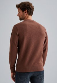 Smeđi dukserica s okruglim izrezom, izrađena od teksturirane tkanine, s rebrastim manžetama i donjim rubom, te malim logom na lijevom ramenu.