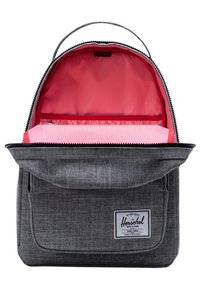 Mochila de tela gris con una textura suave, que presenta un interior de rayas rojas, cierre con cremallera y un bolsillo con solapa que tiene una etiqueta.