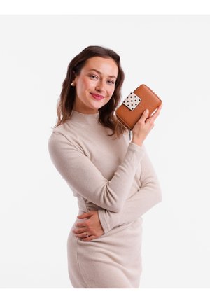 Brown textured wallet with a white clasp featuring black polka dots. The wallet is held in a woman's hand against a white background.