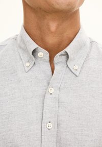 Camicia grigia chiara con tessuto testurizzato, caratterizzata da un colletto a punta e quattro bottoni bianchi sulla chiusura.