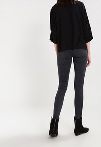 Camiseta negra de gran tamaño con mangas de tres cuartos combinada con jeans skinny gris oscuro. Botines negros con detalle de cremallera.