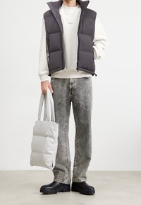 Pehmeä harmaa liivi korkealla kauluksella, beige collegepaita, vaaleanharmaa kangaskassi, kuluneet harmaat farkut ja massiiviset mustat saappaat.