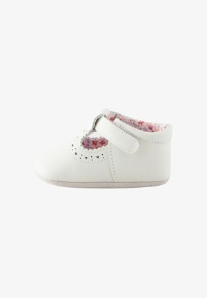 Scarpa bianca in pelle dalla forma arrotondata, con ritagli decorativi sulla parte superiore e foderatura morbida con motivo floreale. Fissata con una fascia in velcro.
