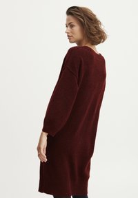 Abito maglione oversize in bordeaux, realizzato in morbido knit, con scollo rotondo e maniche lunghe, caratterizzato da una silhouette rilassata e spacchi laterali.