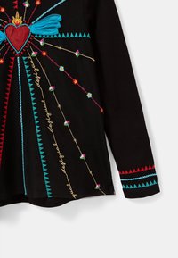 Czarny top z misternym haftem w motyw serca i kolorowymi akcentami, w tym niebieskimi wstążkami, wzorami w zygzak oraz detalami kwiatowymi.