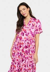 Rosa blommig klänning med korta ärmar, V-ringning, lagerdesign och ett mönster av lila och orange blommor på en ljus bakgrund.