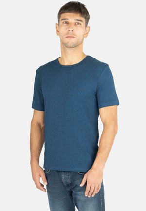 Dark blue crew neck t-shirt made of cotton, short sleeves, and a subtle chest logo detail. Worn with blue denim jeans.