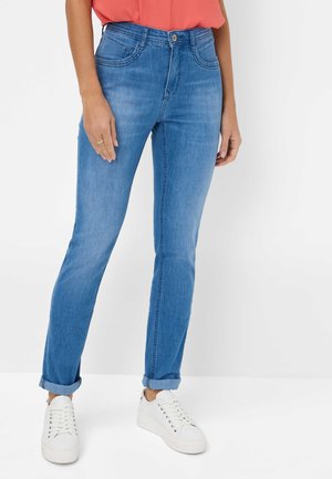 Jeans in denim blu con vestibilità dritta, dotati di orli arrotolati, tasche frontali e chiusura con bottone. Indossati con sneakers bianche.