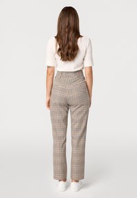 Hoge taille geruite broek in beige en bruin met een textuurafwerking. Kenmerkt zich door een rechte pijp en achterzakken, gecombineerd met witte schoenen.