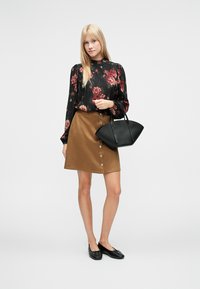 Svart blomstret bluse med lange ermer, brun semsket A-linje skjørt med knappedetalj, svart håndveske og svarte flate sko. Enkel og strukturert.