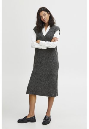 Abito senza maniche lavorato a maglia grigio con una texture a costine, scollo a V e vestibilità morbida, abbinato a una camicia bianca e mocassini neri.