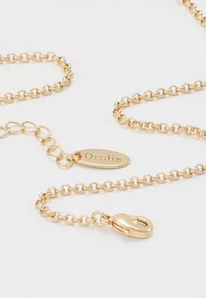 Collier chaîne en or avec fermoir mousqueton et plaque ovale gravée "Orelia" sur fond blanc.